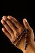 Image of close up of hands of african american woman praying with rosary