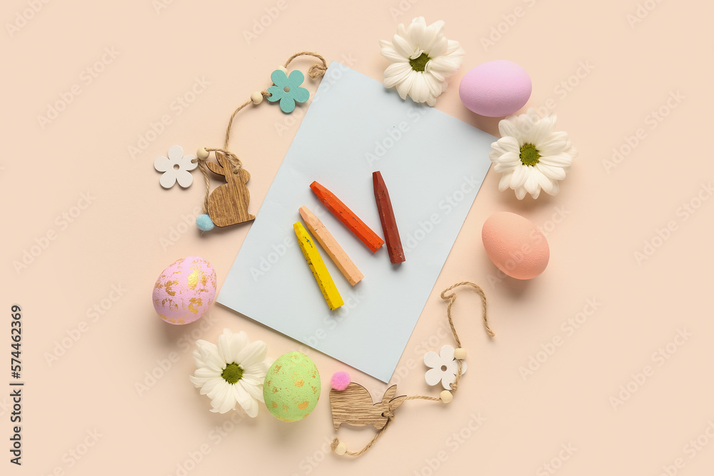 Paper sheet with chalks, Easter eggs and flowers on beige background
