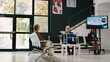 © DC Studio - Elderly man with walking frame sitting in waiting room, talking to woman before attending medical consultation with specialist. Senior person waiting in hospital reception lobby. Tripod shot.