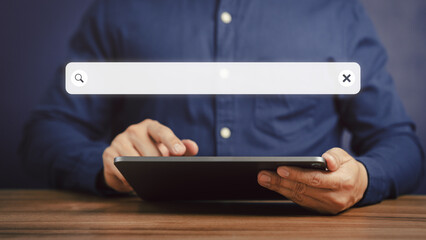 Poster - Adult man hand working with a tablet on the desk in office. Searching browsing internet data information with blank search bar. Search engine optimization SEO networking concept.