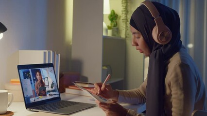 Wall Mural - Young happy Asia muslim woman secretary wear hijab casual clothing video conference meeting on laptop computer with businesswoman at home overtime working at night. Online learning concept.