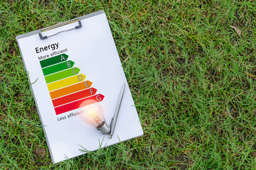 Wall Mural - A light bulb is placed on a piece of paper that indicates the energy efficiency rating of an appliance indicating how much electricity it should save.laying on the green lawn