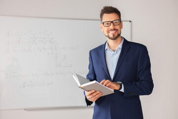 Wall Mural - Happy teacher with book at whiteboard in classroom during math lesson