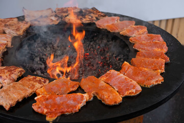 Process of cooking fresh juicy meat steaks on brazier at summer local food market - close up view. Outdoor cooking, gastronomy, cookery, street food concept