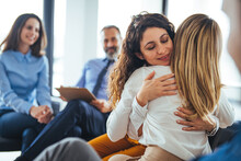 Young Adult Woman Embracing And Supporting Friend During Support Group Therapy Session With Diverse Women. Two Women Hug In Therapy Session. Group Therapy Session, Empathy Concept