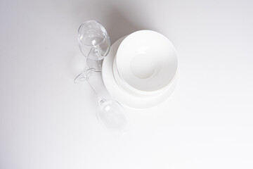 Wine glasses and white plates, bowls on white table. Table setting for dinner