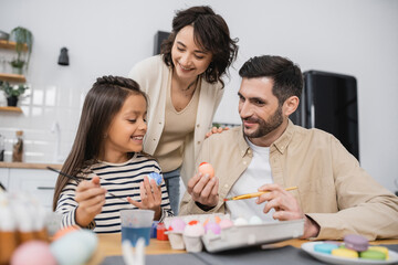 happy parents looking at daughter coloring Easter egg at home.