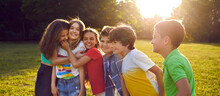 Happy Kids Enjoying Summertime, Playing Outside And Having Fun Together. Group Of Joyful Little Friends Walking In Green Park And Hugging Each Other. Header Background. Children And Friendship Concept