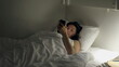 © Marco - Woman looking at cellphone device laying in bed at night. Female person staring at glowing screen in the dark before bedtime