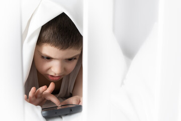 Wall Mural - A 5 year old boy plays games on his phone while lying in bed. Gadgets in bed before bedtime in a child