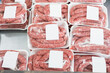 Raw pork sausages packed in plastic trays wrapped in film with labels offered for sale in butcher shop display.