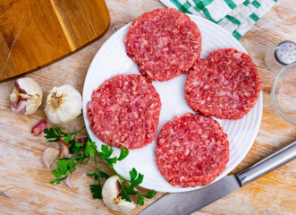 Wall Mural - Shaped patties for burgers from raw ground beef meat with fresh parsley sprigs, spicy garlic and allspice on plate. Cooking ingredients