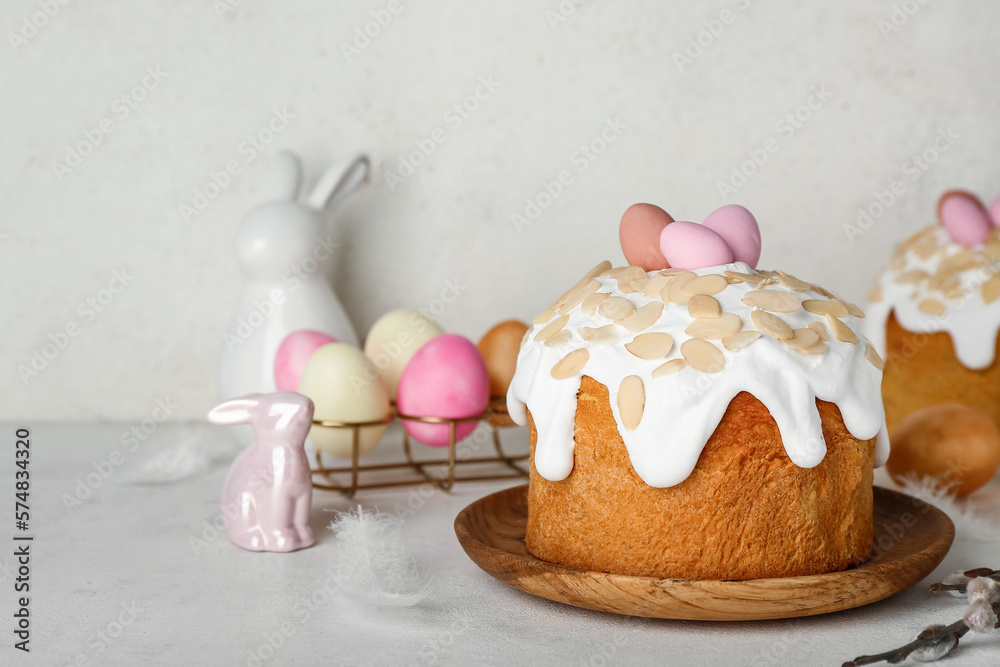 Easter cake, painted eggs and bunnies on table near white wall