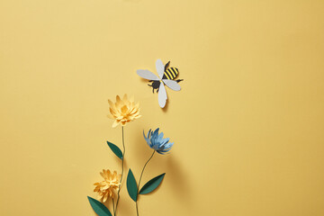flowers with many colors and a paper bee on light yellow background. empty area for product or text.