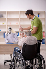 Wall Mural - Old patient in wheel-chair visiting skeleton doctor
