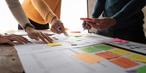 Close up ux developer and ui designer brainstorming about mobile app interface wireframe design on table with customer brief and color code at modern office.Creative digital development agency.panning