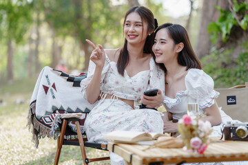 Wall Mural - Two pretty asian friends woman picnic at park outdoor in relax time holiday, holiday recreation concept.