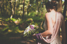 A Young Woman Holds A Bouquet Of Flowers In A Forest Setting.