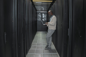 Leinwandbilder - Laptop, network and data center with IT black man for research, engineer working in dark server room. Computer, cybersecurity and analytics with male programmer problem solving or troubleshooting