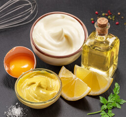 Wall Mural - Homemade mayonnaise and mayo ingredients on black stone slate serving plate close-up.