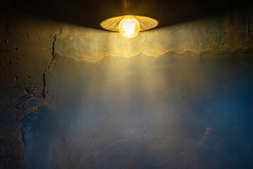 Background from a blue house wall with brittle plaster in the dark illuminated by a light bulb from above. An empty scene lit by a cone of light.