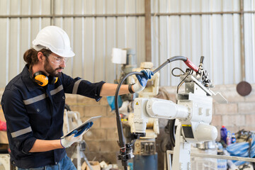 Wall Mural - Male engineer worker working with tablet for control welding robot arm in workshop. Male engineer maintenance automatic welding robot arm in factory. Industry robot manufacturing technology