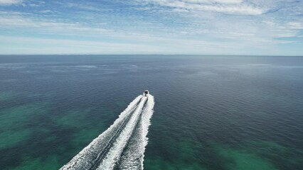 Wall Mural - Boat on the sea. Aerial video of a drone following a boat leaving the pier. Location Shark Bay in Western Australia. Ocean view from the sky and white foam. Boat cruising in high speed.