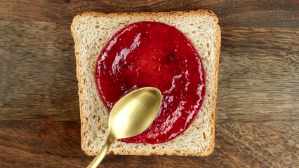 Wall Mural - Raspberry jam spreading on bread with a golden spoon, top view. Perfect traditional breakfast