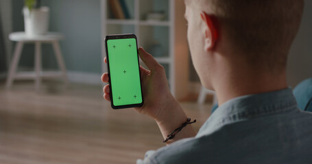Wall Mural - Man using a mobile phone with chroma key green screen, watching a video or having an online conference - technology, communications concept close up