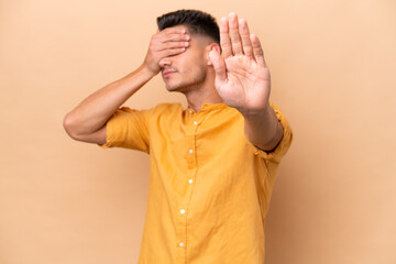 Wall Mural - Young caucasian man isolated on beige background making stop gesture and covering face