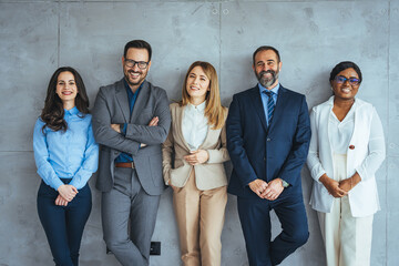 Studio portrait of a group of businesspeople posing against a gray background. Portrait of multi-ethnic male and female professionals. Business colleagues are standing against wall.