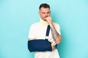 Wall Mural - Young caucasian man wearing a sling  and neck lace isolated on blue background having doubts