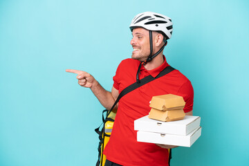 Wall Mural - Young caucasian man with thermal backpack and holding fast food isolated on blue background pointing finger to the side and presenting a product