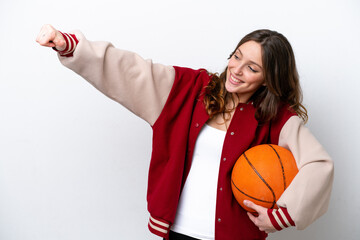 Wall Mural - Young caucasian woman playing basketball isolated on white background giving a thumbs up gesture