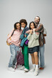 © LIGHTFIELD STUDIOS - full length of cheerful multiethnic students in trendy clothes posing with backpacks on grey background.