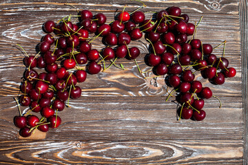 Many ripe red cherries on twigs lie on the edge of a wooden table with a striped texture. An interesting image for your design, creative or illustrations.