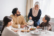 © LIGHTFIELD STUDIOS - African american woman in hijab pouring milk near family during suhur breakfast at home.