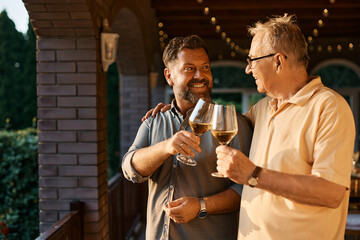 Wall Mural - Happy man and his senior father toast with wine after family lunch on patio.