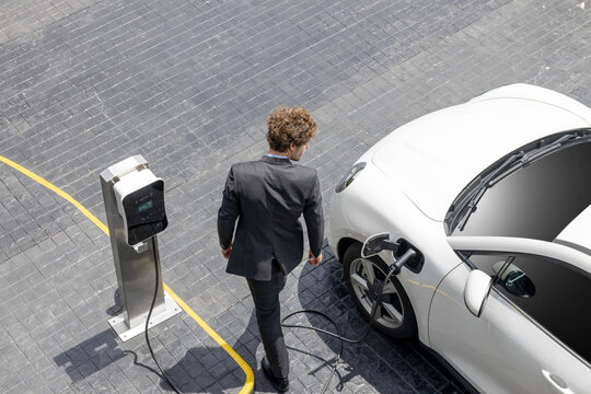 aerial view of progressive businessman in black formal suit with his electric vehicle recharging bat