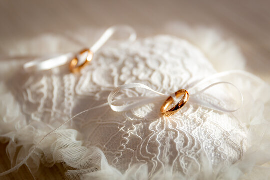 Precious gold wedding rings resting on an elegant white lace cushion