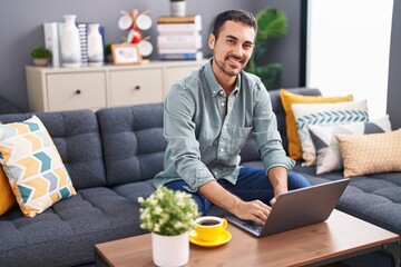 Poster - Young hispanic man using laptop drinking coffee at home