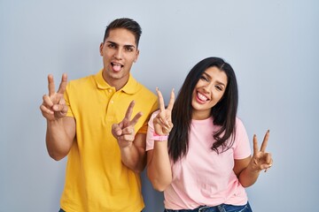 Poster - Young couple standing over isolated background smiling with tongue out showing fingers of both hands doing victory sign. number two.