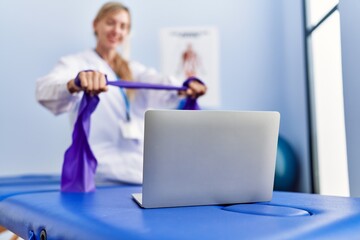 Wall Mural - Young blonde woman wearing physiotherpist having online recovery session at physiotherapy clinic