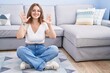 © Krakenimages.com - Young caucasian woman sitting on the floor at the living room showing and pointing up with fingers number nine while smiling confident and happy.