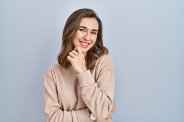 Canvas Print - Young woman standing over isolated background looking confident at the camera smiling with crossed arms and hand raised on chin. thinking positive.