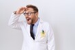 © Krakenimages.com - Middle age doctor man with beard wearing white coat very happy and smiling looking far away with hand over head. searching concept.