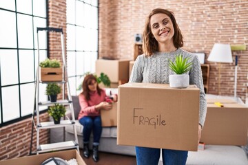 Canvas Print - Mother and daughter moving to a new home holding cardboard box smiling with a happy and cool smile on face. showing teeth.