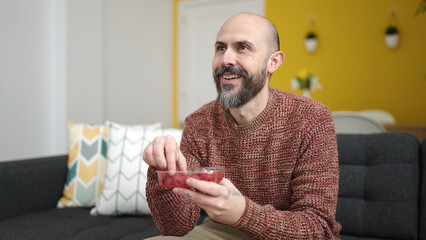 Sticker - Young bald man eating raspberries sitting on sofa at home