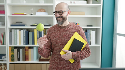 Wall Mural - Young bald man teacher holding books and apple at university classroom