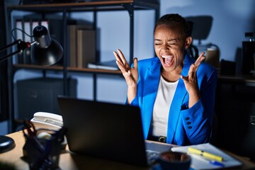 Sticker - Beautiful african american woman working at the office at night celebrating mad and crazy for success with arms raised and closed eyes screaming excited. winner concept